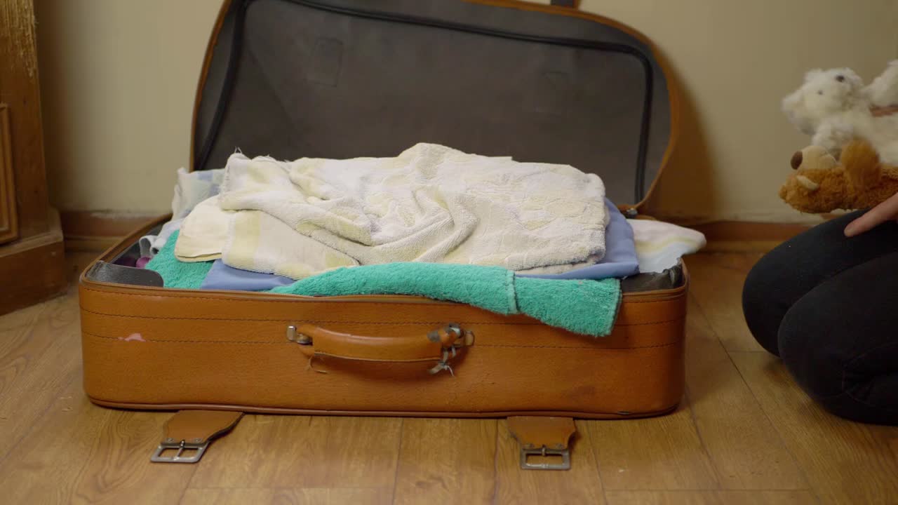 Parent packing children's toys into a suitcase wide shot