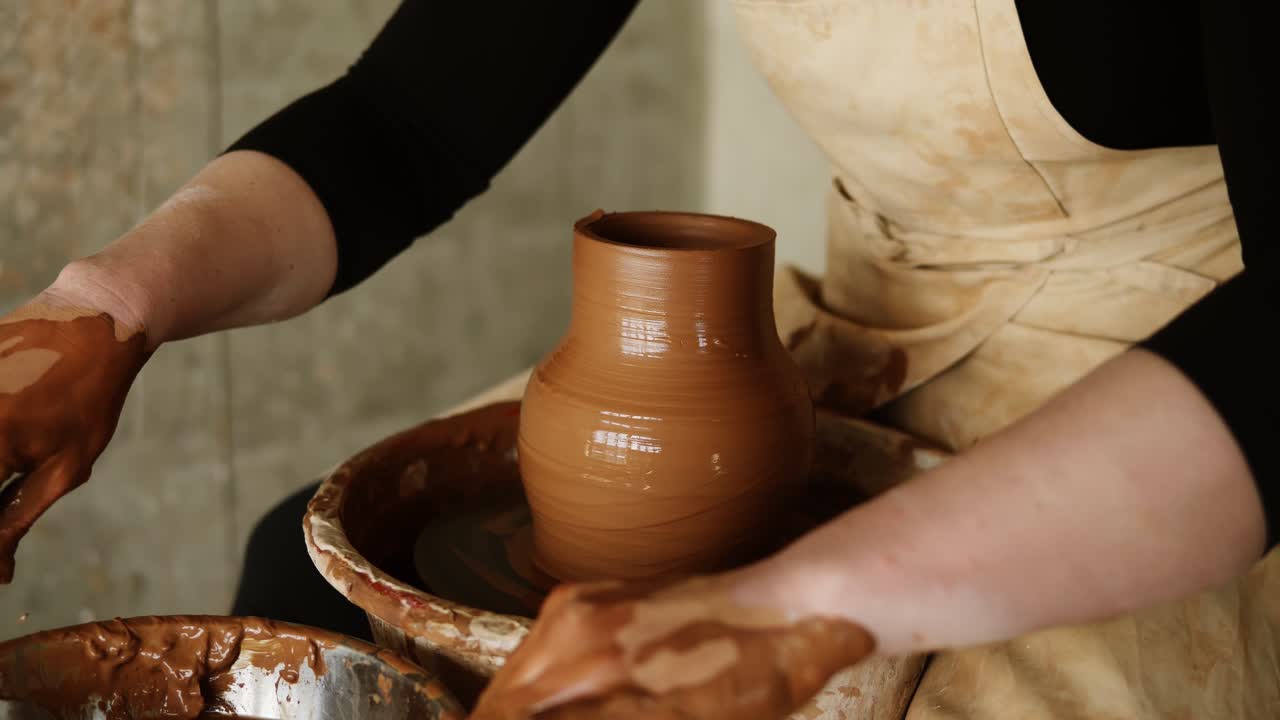 Female potter cuts off excess clay on the top of the vase. Creating vase of clay close-up. Girl makes cup out of clay closeup. Twisted potter's wheel. Women's hands making clay vase