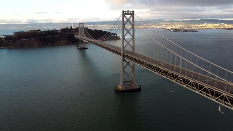 Imágenes-Aéreas-De-Drones-De-4k-30fps-Del-Puente-De-La-Bahía-De-San-Francisco-Oakland,-Isla-De-Yerba-Buena:-Los-Automóviles-Viajan-Por-La-Carretera,-Nubes-Tormentosas,-Aguas-Tranquilas-De-La-Bahía,-Puesta-De-Sol-Que-Se-Refleja-En-Las-Olas,-Arquitectura-De-Récord-Mundial