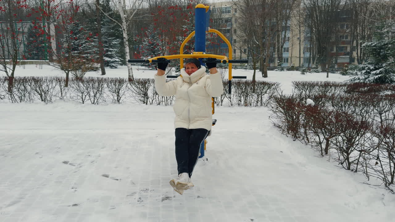 Positive adult woman doing sport in winter. Training on the simulator outdoors. Healthy lifestyle.