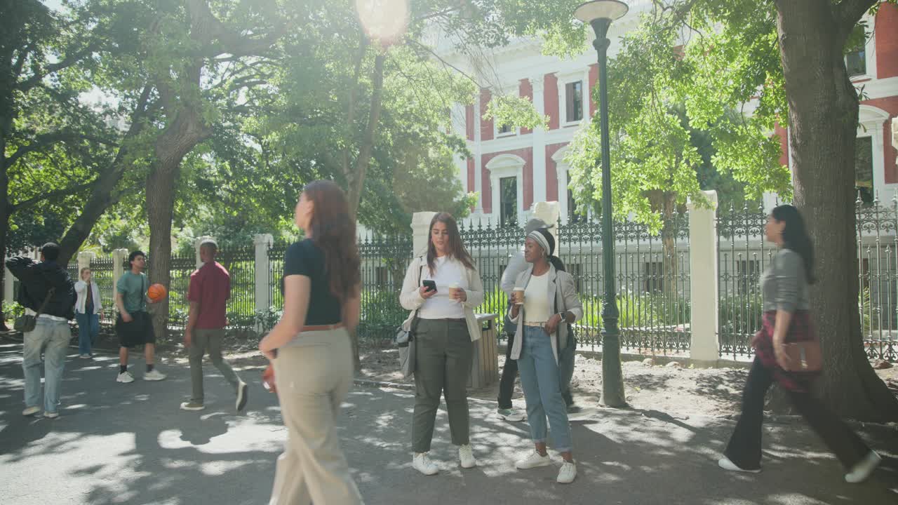 アフリカ系アメリカ人女性たちがカップを手に道を歩き、スマートフォンを確認しながら、赤と白の建物のそばでセルフィーを撮っている。