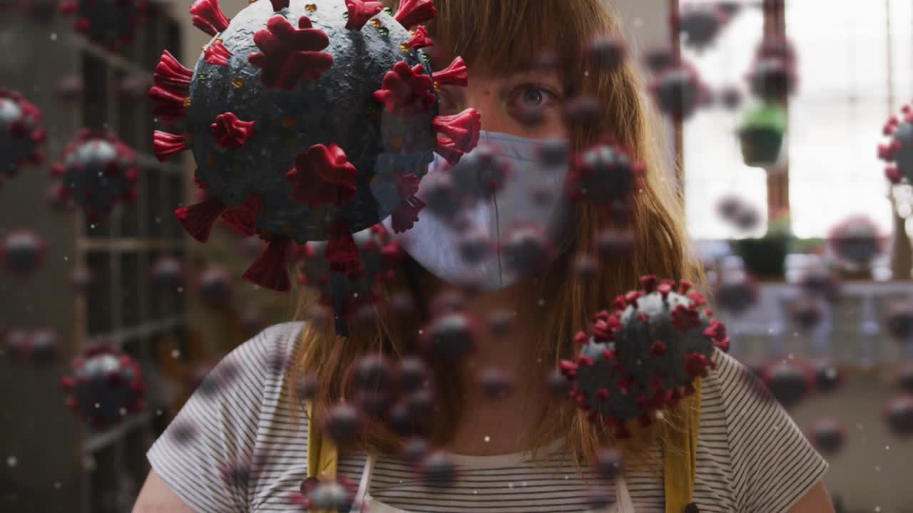 Donna di mezza età che sistema il grembiule e poi la mascherina in un negozio mentre modelli di virus fluttuano, causando preoccupazione per la salute