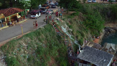 Dolly-in-aerial-drone-shot-of-tourists-watching-the-sunset-from-the-famous-outlook-in-the-tropical-beach-town-of-Tibau-do-Sul-covered-in-palm-trees-and-exotic-foliage-in-Rio-Grande-do-Norte,-Brazil