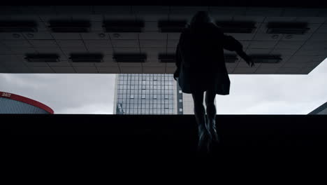 Woman-going-up-stairs-from-dark-underground-metro-station-in-city-centre.