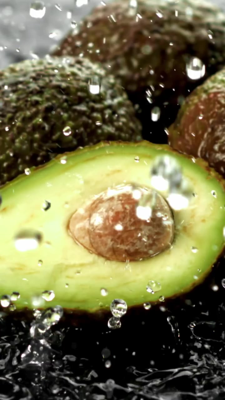 Primo piano di avocado fresco tagliato a metà con gocce d'acqua che schizzano