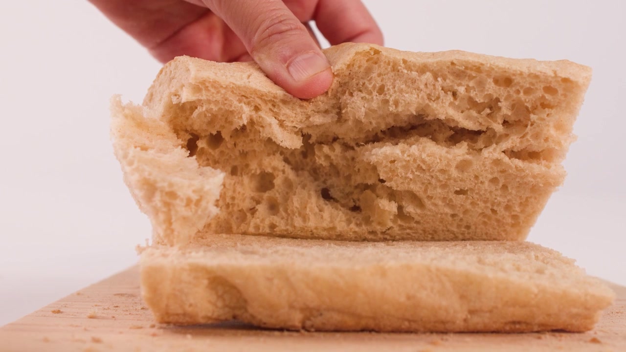 Close-up shot of hands separating a sliced loaf of crusty sourdough bread on wood.
