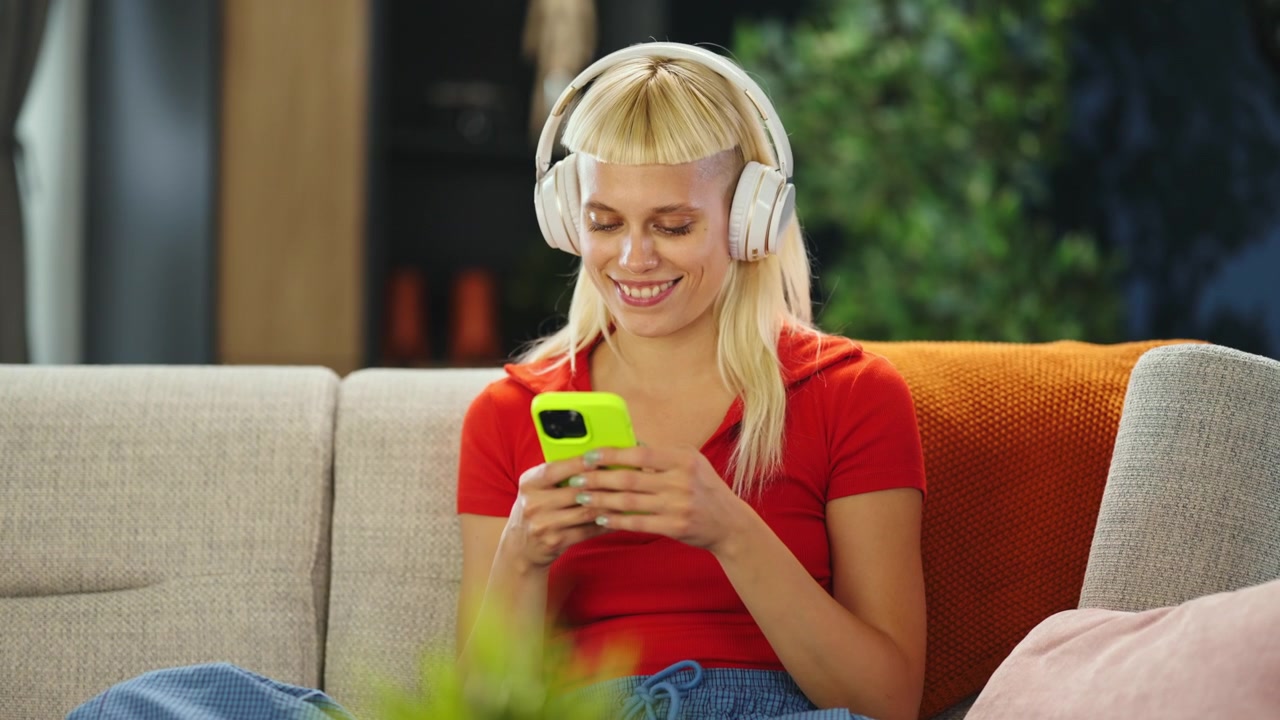 Giovane donna con le cuffie che usa lo smartphone sul divano