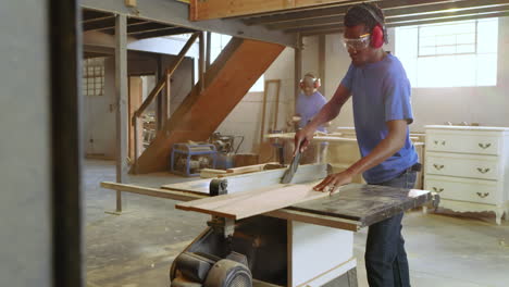 mid black male carpenter entering workshop cutting board on table saw while team cutting boards