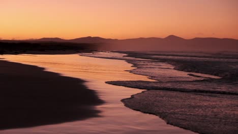 stunning beach scene with orange sky at twilight as waves roll onto reflective sand