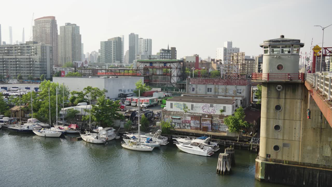 도크 된 항해 보트 의 줄 들 이 평화롭게 휴식 하고 있는 가운데, 강 통로 의 물 이 다리  ⁇  에 흐르고 있으며, 도시 의 스카이 라인 에 틀어져 있다