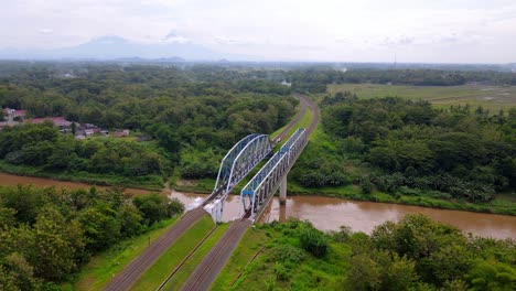 Drone-view-of-a-two-lane-train-rail-over-a-river-in-rural-Magelang,-Central-Java