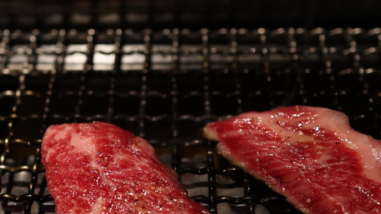 Detailed view of marbled beef slices sizzling on a grill, showcasing texture and cooking process.