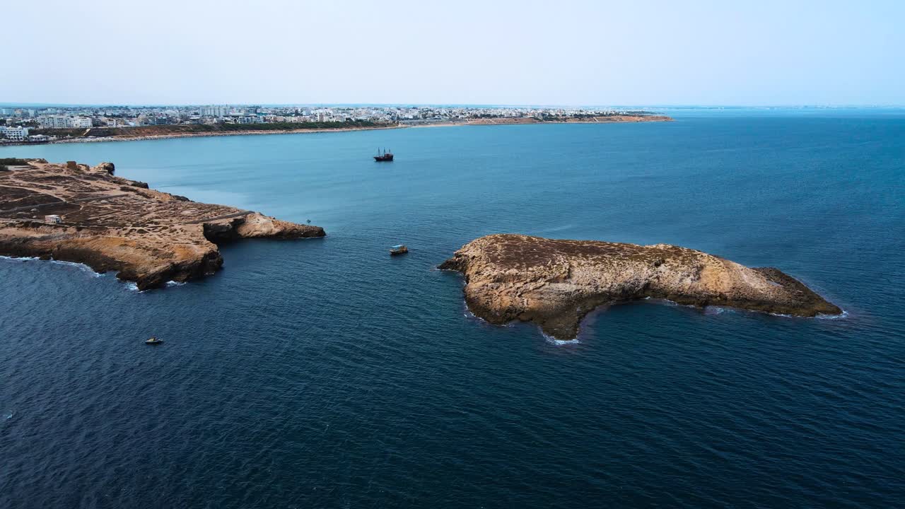 A beautiful ocean scene with blue water and rocks in the background. There is a boat out in the water on the left side of the image.