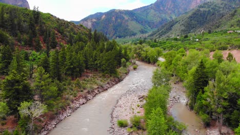 flowing river with rocky riverbanks surrounded by green pine coniferous trees and alpine woodland rocky mountains