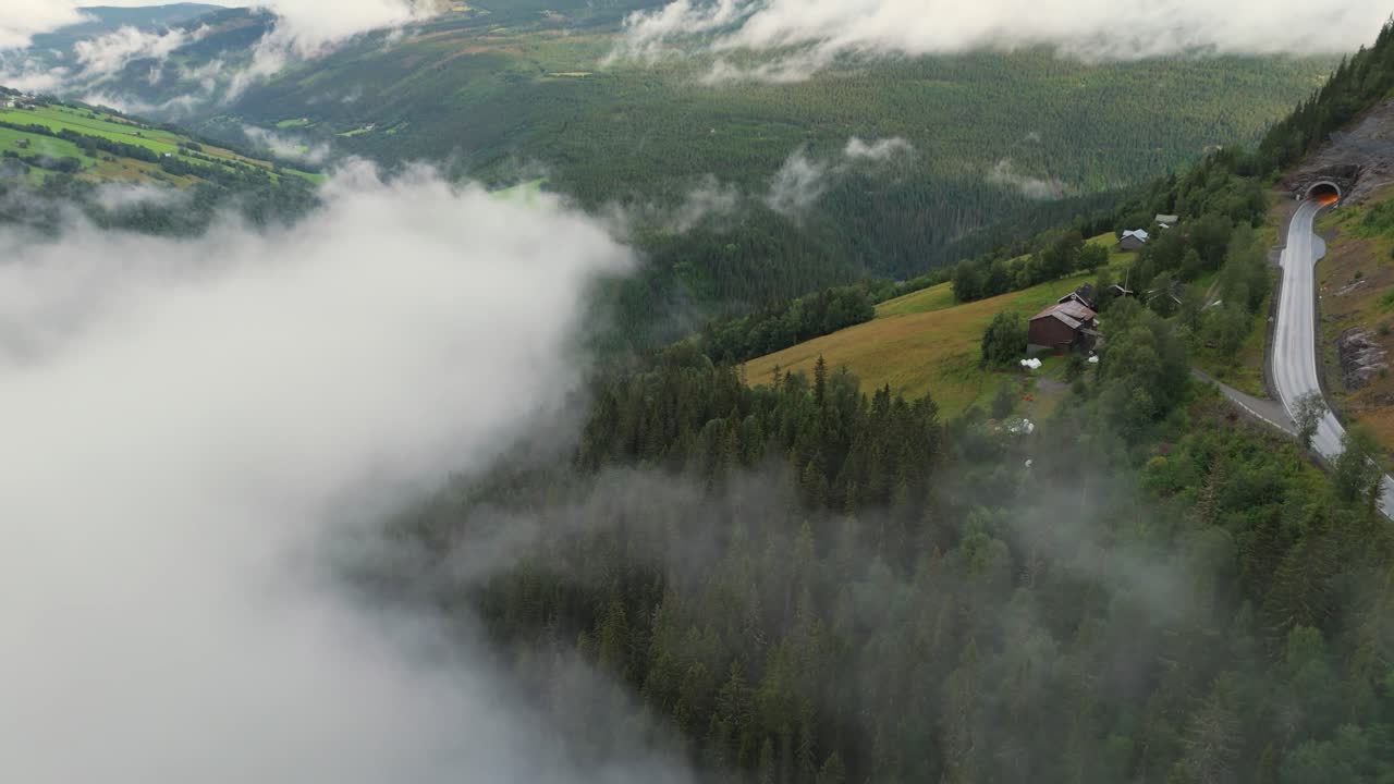 vista aérea de las nubes sobre un bosque y una sinuosa carretera de montaña, capturando la belleza natural y el paisaje sereno