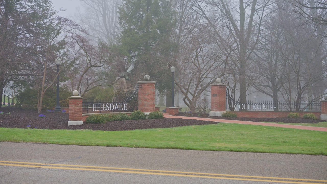 Cinematic boom up shot from across the road revealing Hillsdale Michigan college sign with campus setting and surroundings.