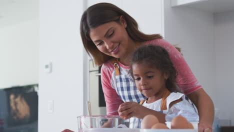 Madre-E-Hija-Hispanas-Rompiendo-Huevos-En-Un-Tazón-Mientras-Hornean-Pastel-En-La-Cocina