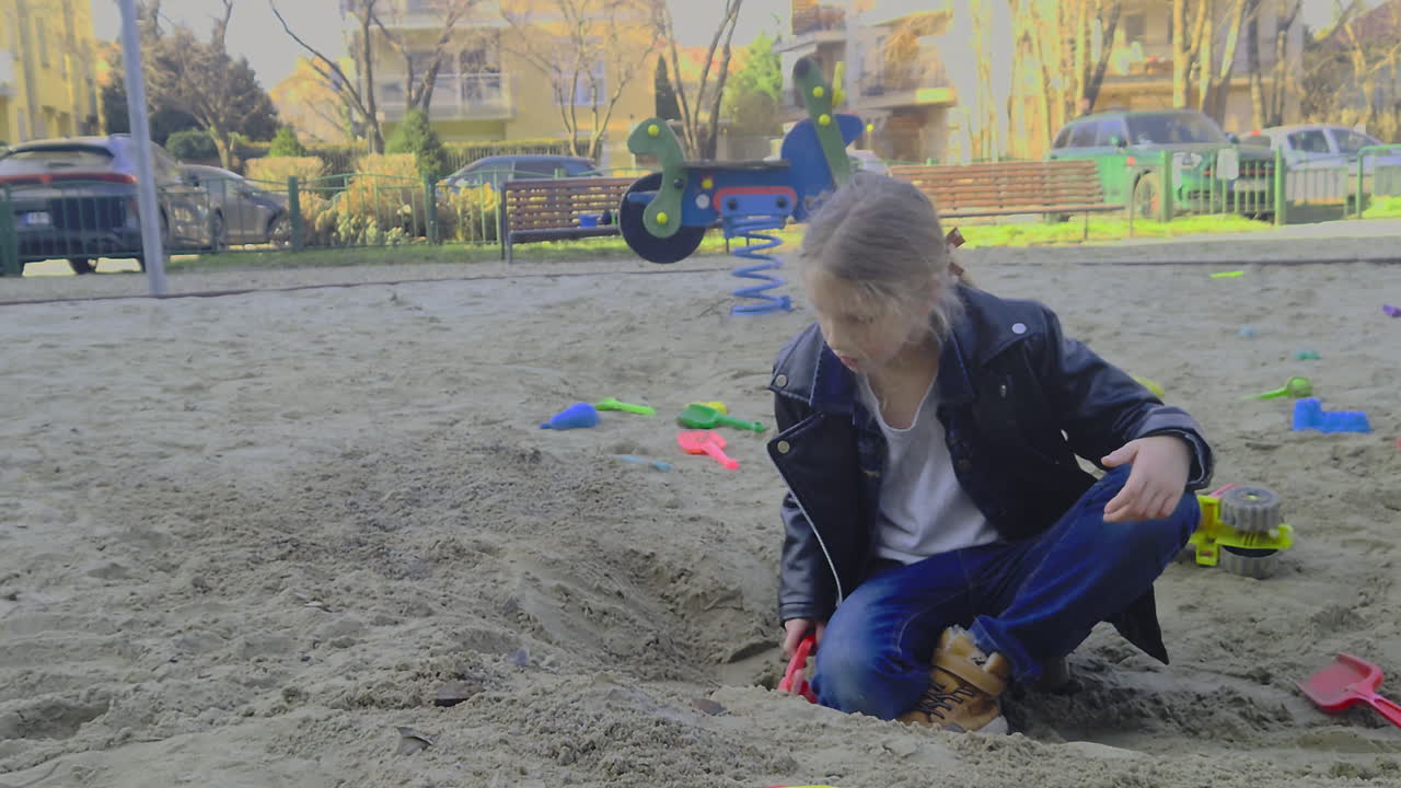 Cinematic downward move on a girl in a leather jacket digging in a sandbox. Features natural color grade and sharp lifestyle details in a 2026 style