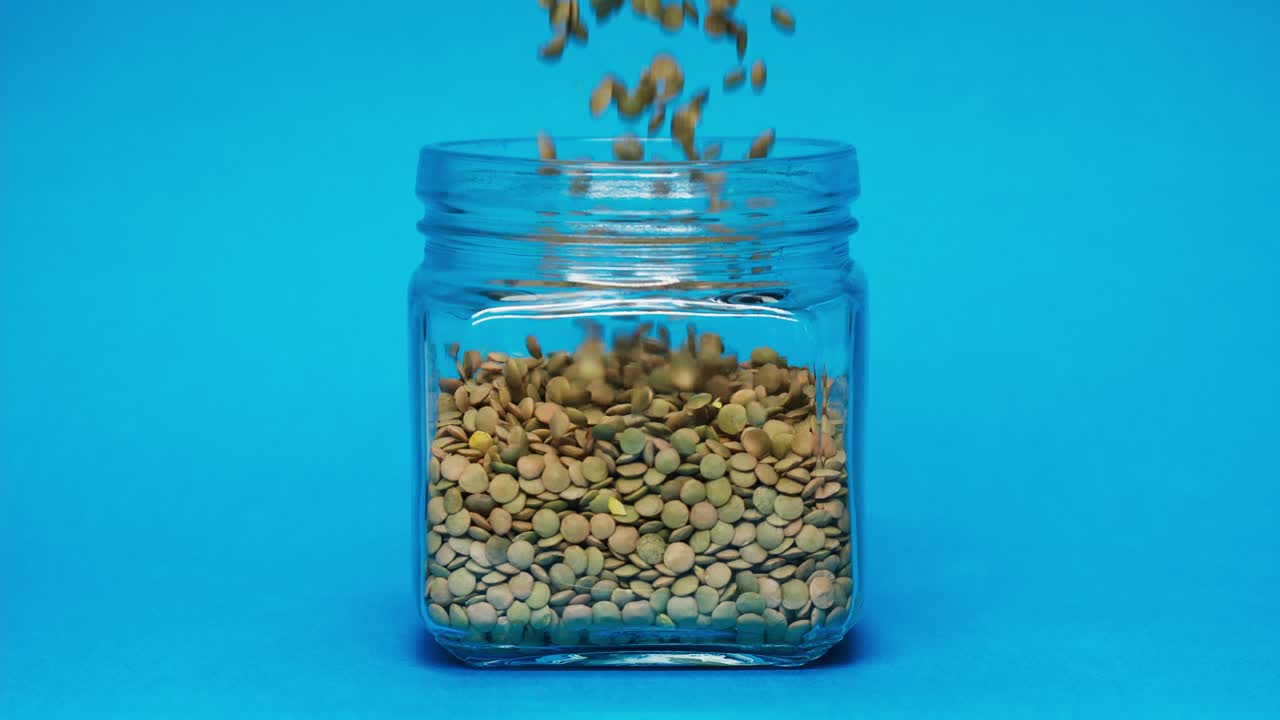 Linsen fallen in ein Einmachglas auf blauem Hintergrund.