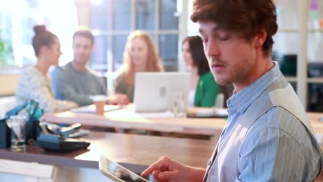 Casual-businessman-using-tablet-computer-with-his-colleagues-behind-him