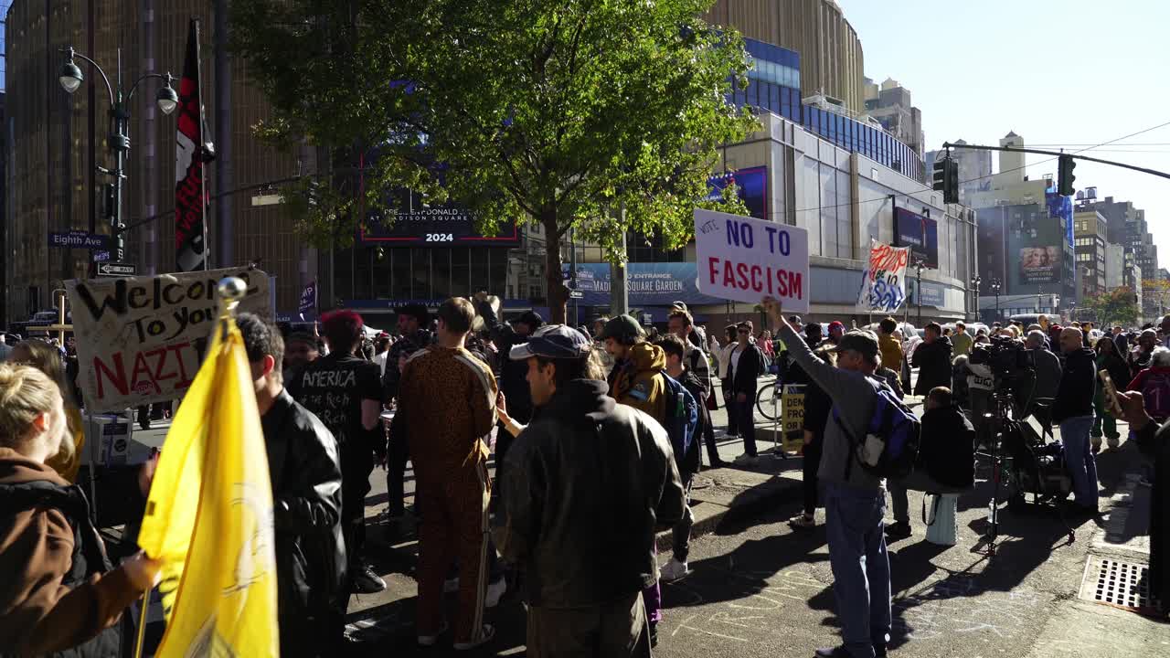 The sun shines brightly on the crowd gathered near Madison Square Garden, where protesters chant and hold signs in protest of Trump