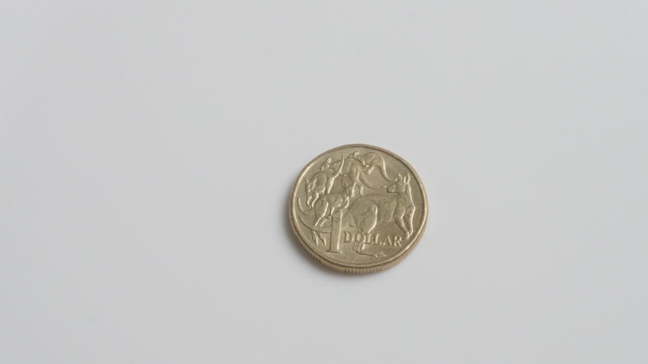 Una singola moneta d'oro che gira su una superficie bianca prima di fermarsi. Moneta australiana da un dollaro AUD.