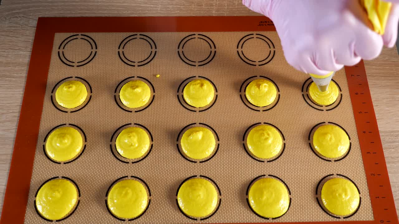 el chef de pastelería está cocinando macarrones. vertiendo masa en la alfombra de silicona de plantilla.