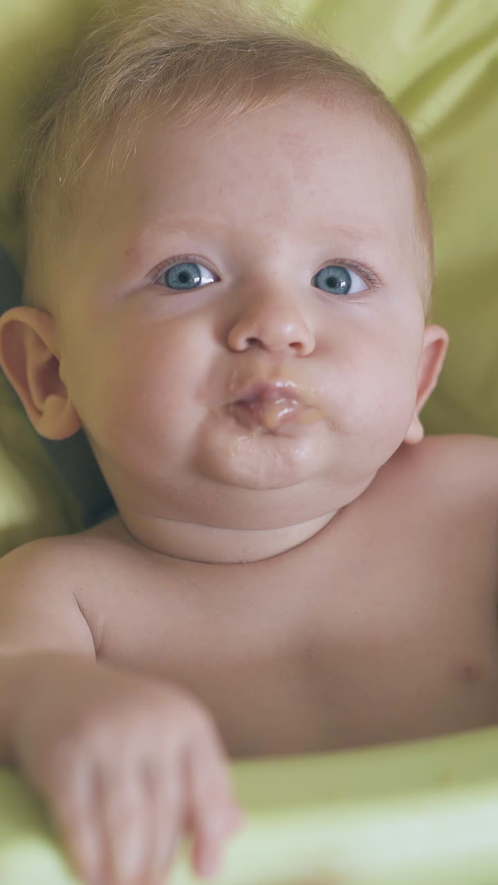 young mommy feeds adorable baby with tasty cream soup in soft green highchair in light room extreme close view