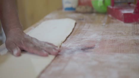 un chef de pastelería golpea la masa con las manos y luego alcanza a través del mostrador para una herramienta o ingrediente