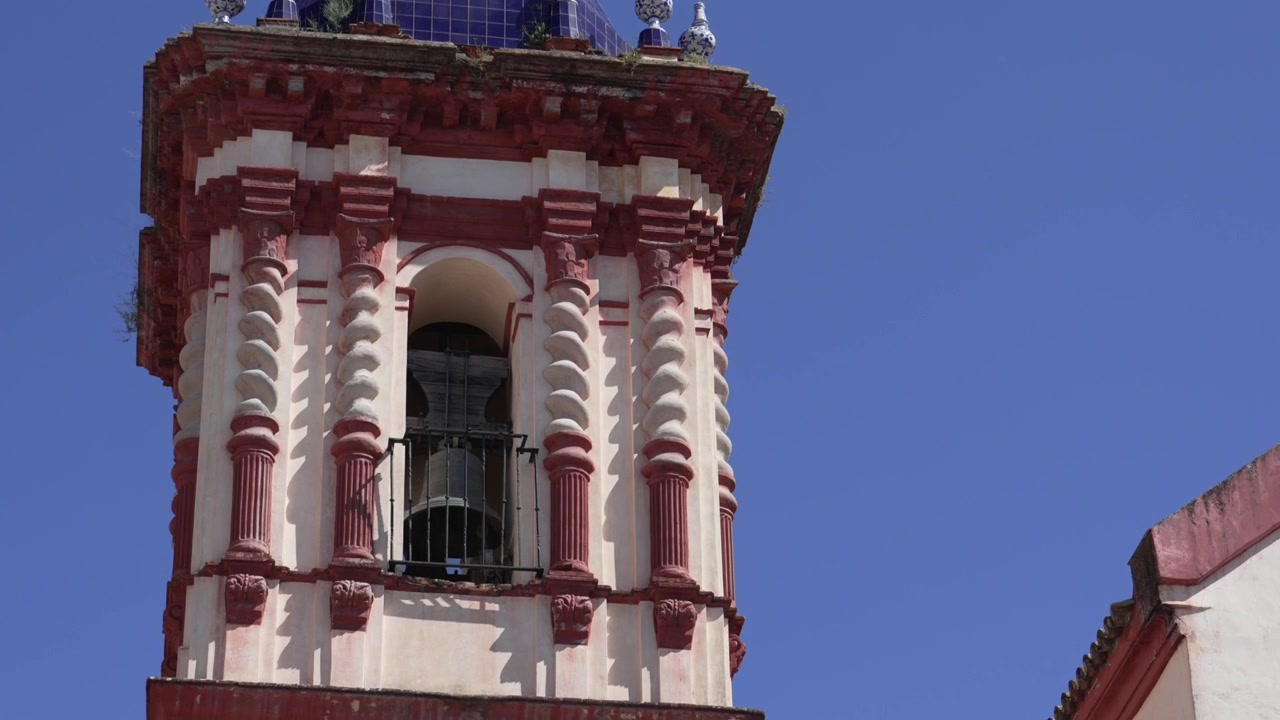 Storica torre campanaria con facciata ornata rossa e bianca a Siviglia