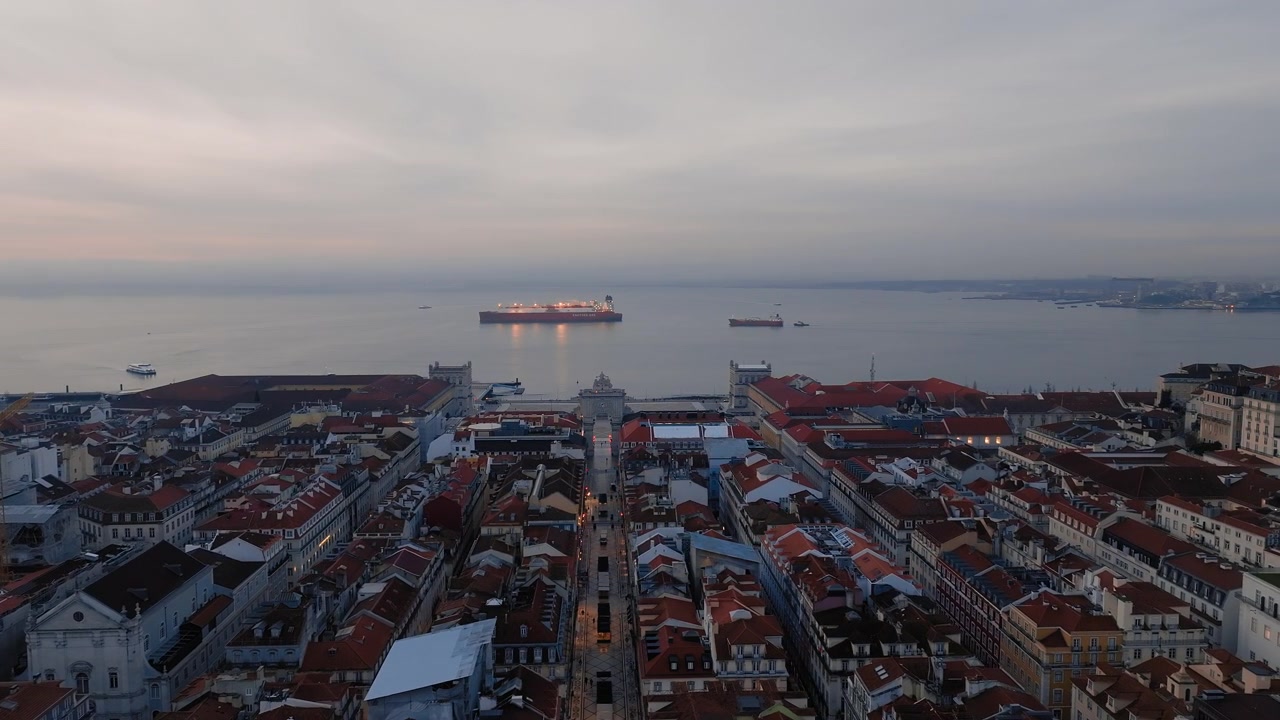Ripresa drone panoramica lenta di Piazza del Commercio, Lisbona, all'alba. Cielo coperto, nebbia all'orizzonte. Navi cisterna sul fiume Tago. Portogallo