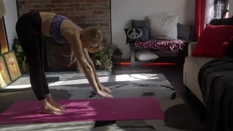 Hermosa-Chica-Blanca-Caucásica-De-Cabello-Rubio-Largo-Y-Flaca-O-Mujer-En-Traje-De-Yoga-Estirándose-Y-Haciendo-Una-Pose-De-Perro-Hacia-Arriba-En-Una-Alfombra-De-Yoga-Rosa-Y-Estirándose-En-Una-Alfombra-Frente-A-La-Chimenea-Del-Apartamento