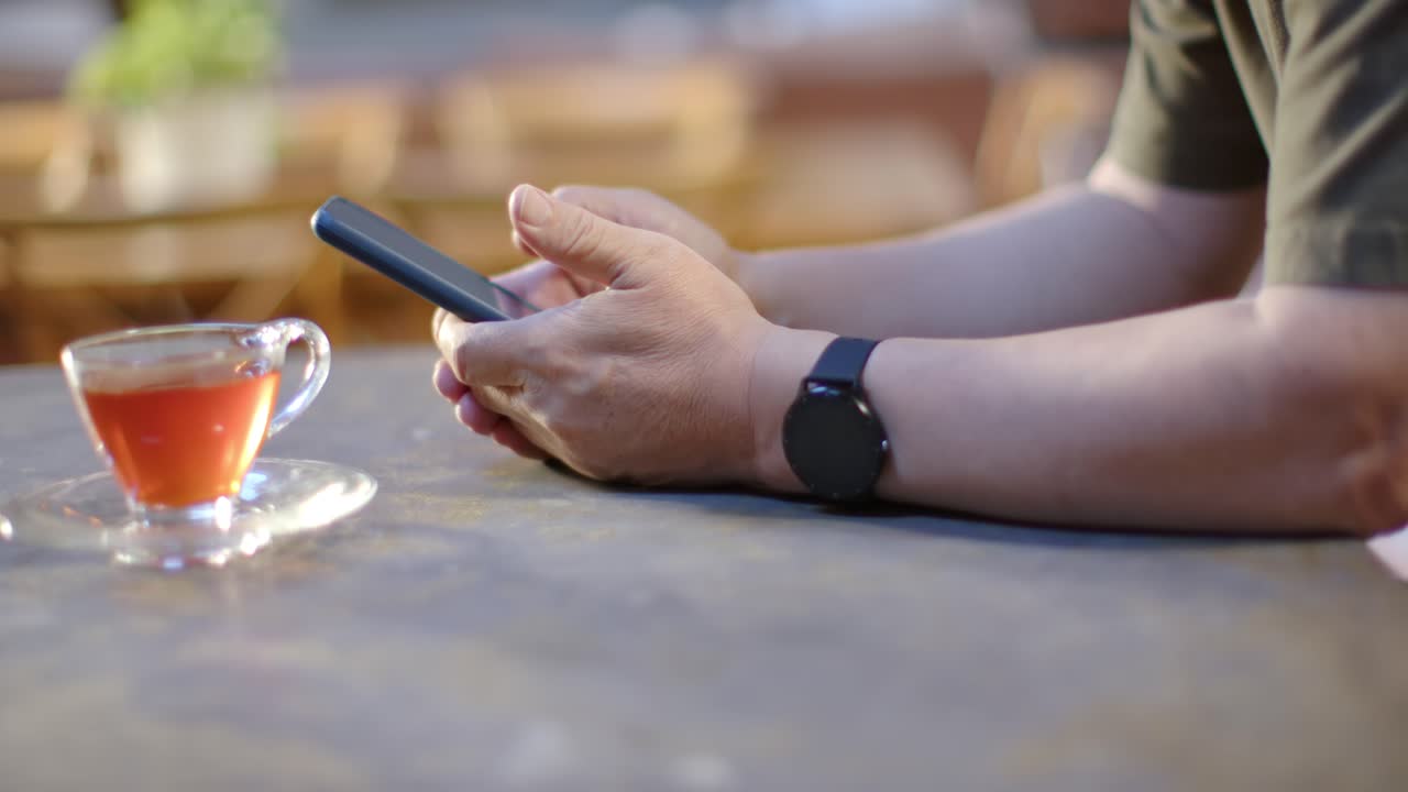 Senior Asian man starting hands resting, holding and swiping phone at table, teacup, watch, texting