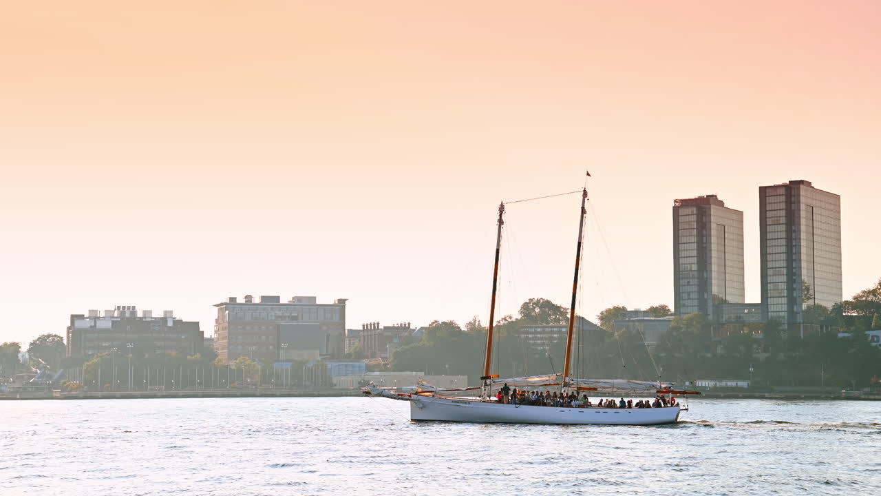 New York, USA, 15 aprile 2026: Yacht a vela sul fiume vicino al lungomare di Manhattan. Grande yacht a vela sul fiume vicino al lungomare di Manhattan durante il tramonto con edifici e luce serale soffusa