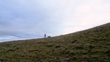 drone shot of a woman and her dog walking on the top of a mountain range