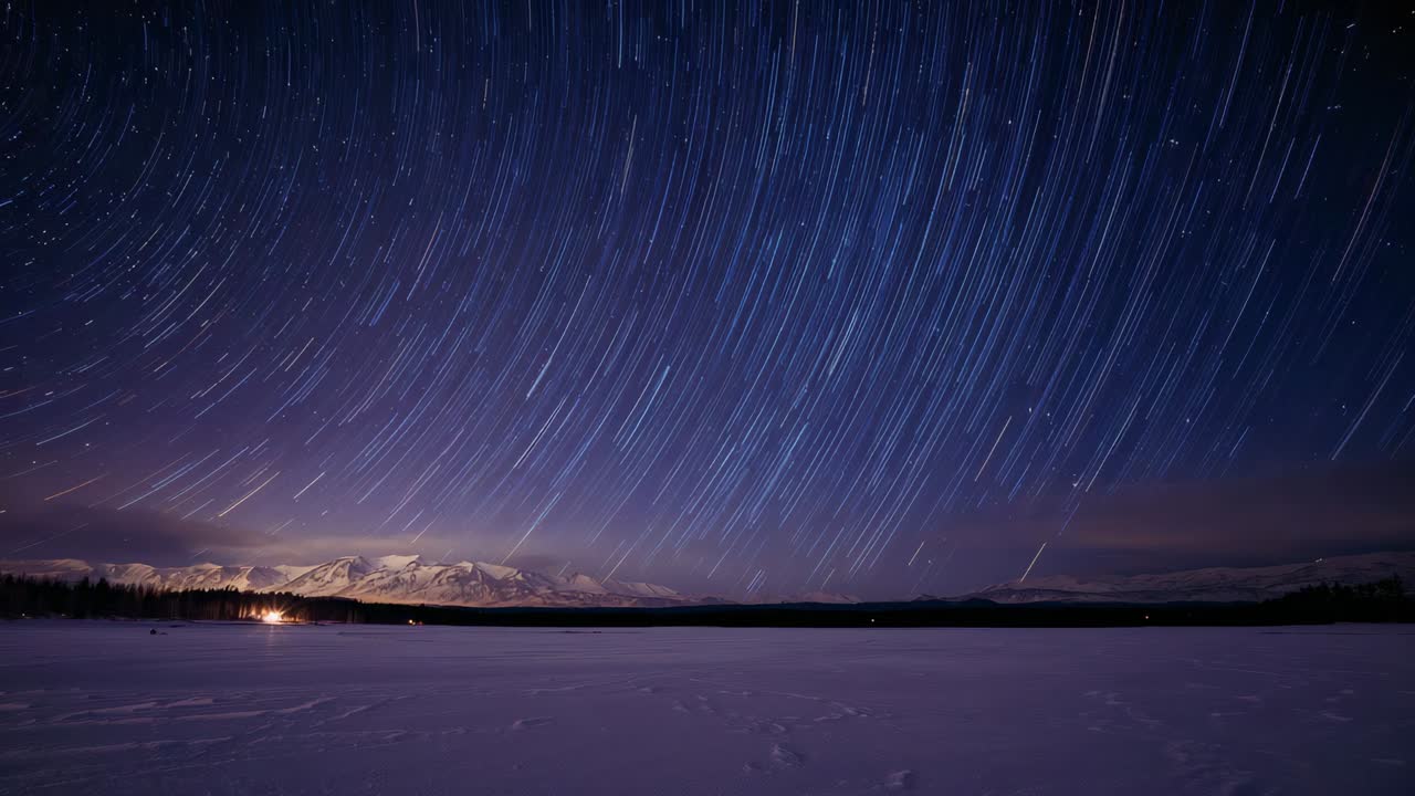 Starting camera timelapse capturing rotating star trails over snowy lake at night with shore light