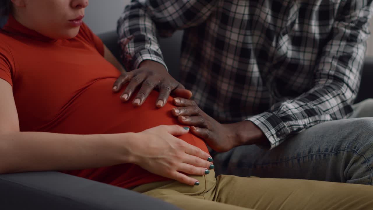 Close up of interracial hands of young couple on belly