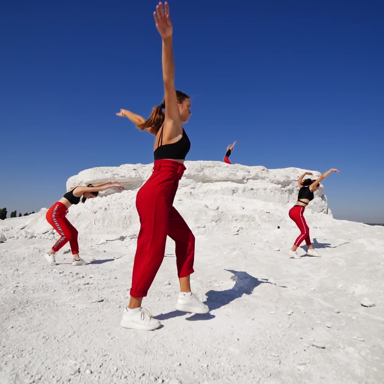 Few girls in the similar outfit dancing outdoors. Dance group performing on the white ground at the backdrop of blue sky. Low angle view