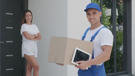 una mujer hermosa se encuentra con un repartidor con una caja de paquetes y una tableta al lado de su casa. concepto de mensajero, entrega a domicilio, compras en línea