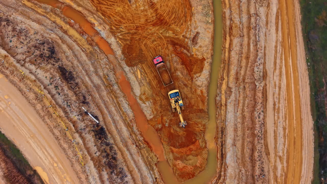 Excavator loading sand into dump truck. Direct overhead shot of heavy equipment working in sand pit near water drainage