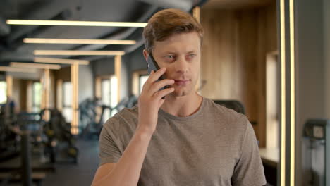 Handsome-sportsman-talking-on-phone-in-sport-club.-Bodybuilder-standing-at-gym.