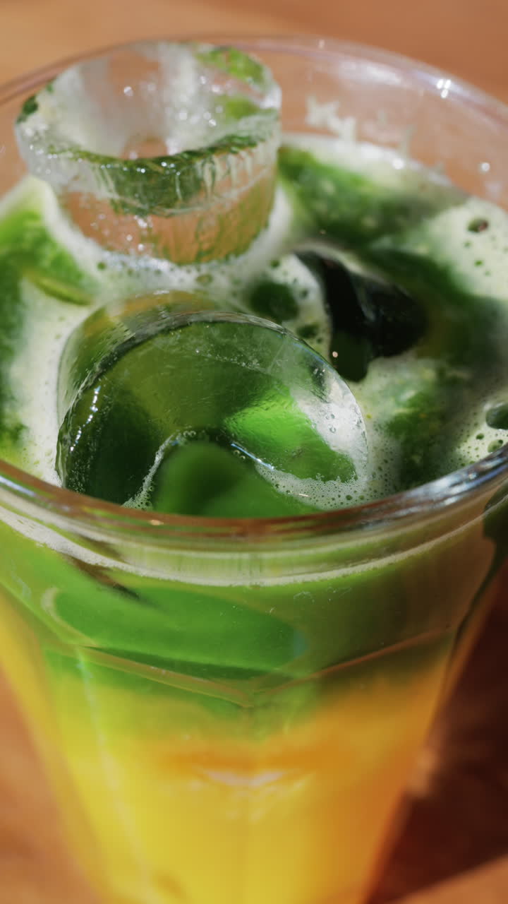 Close up of a glass of an iced orange juice matcha on a table at a cafe. Vertical