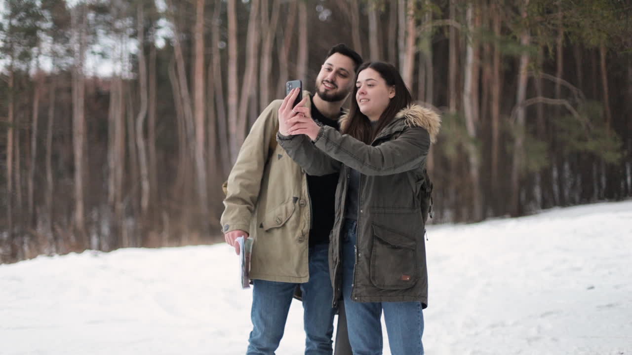 pareja caucásica tomando selfies en un bosque nevado.