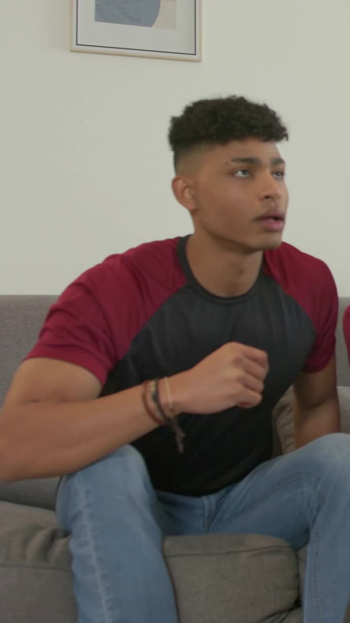 Vertical video: Reacting to offframe action, man in maroon leaning on gray sofa while friend joins