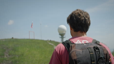 A-young-hiker-with-a-backpack-walking-towards-the-pole-with-Slovenian-flag-on-a-peak-of-mountain-Lisca