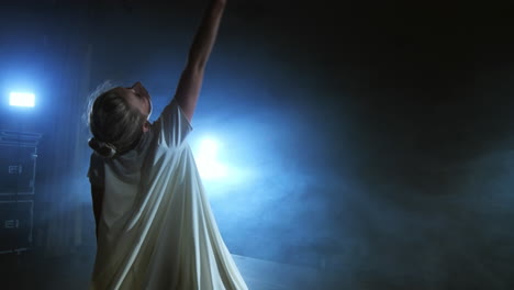 modern dance woman in a white dress dances a modern ballet jumps makes rotation on the stage with smoke in the blue spotlights.