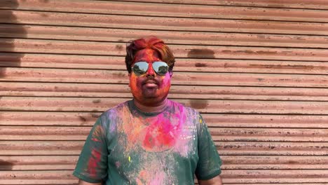 closeup shot of face of a man filled with colors wearing sunglasses on holi