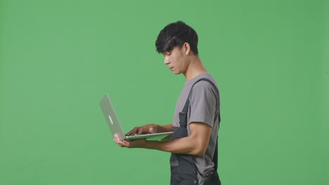 녹색 화면 배경 스튜디오에서 는 동안 노트북을 사용하는 아시아 남성 노동자의 측면 시각