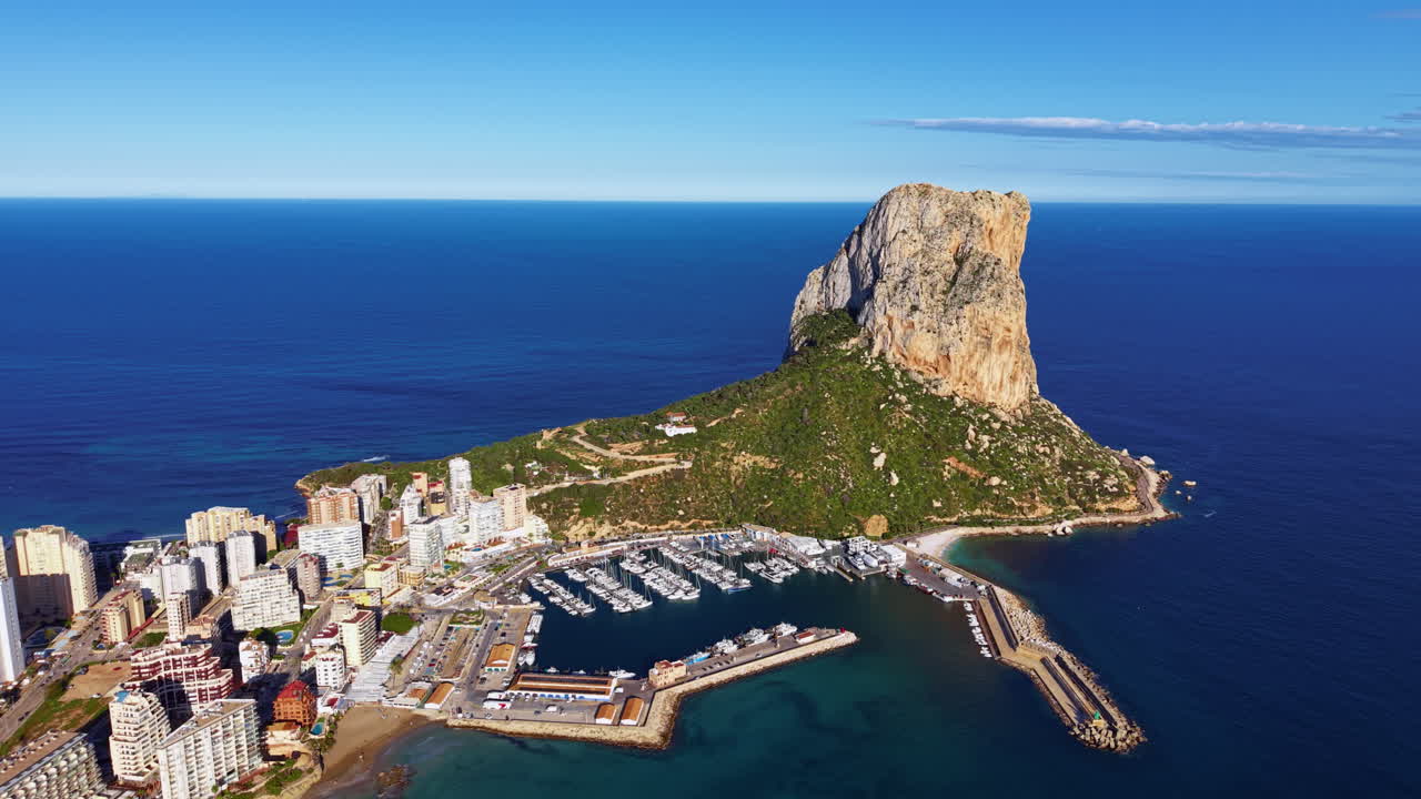 Veduta aerea di Calpe, Spagna, con l'iconica formazione rocciosa Penon de Ifach che si erge sul Mar Mediterraneo, con porto turistico e paesaggio urbano costiero