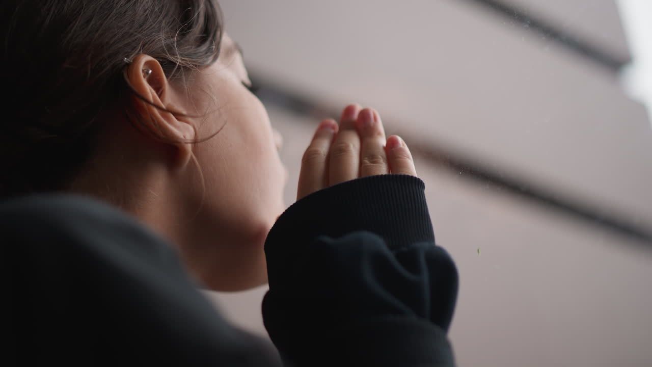Giovane osservatore che guarda attentamente la pioggia scorrere sui vetri in silenzio. Giovane individuo che osserva pazientemente e tranquillamente la pioggia che cade sulle superfici di vetro con calma e meraviglia.